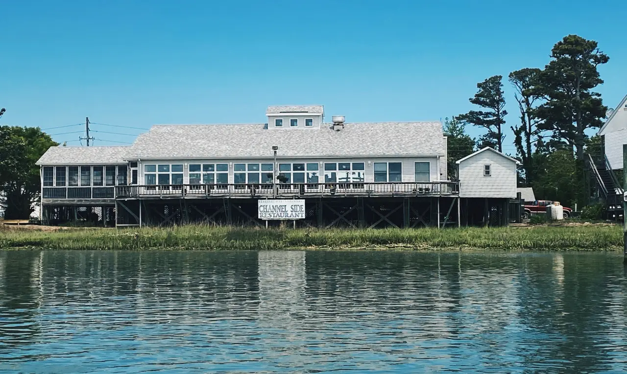 The waterfront restaurant building on East Side Road seen from the channel, its deck full of guests